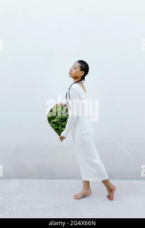 Femme sereine tenant un miroir par un mur blanc Banque D'Images