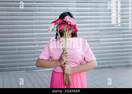 Jeune femme couvrant le visage avec des pâquerettes de Gerbera devant le fer ondulé Banque D'Images