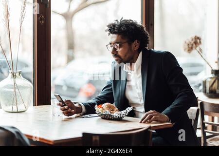 Homme d'affaires utilisant un smartphone tout en déjeunant au restaurant Banque D'Images