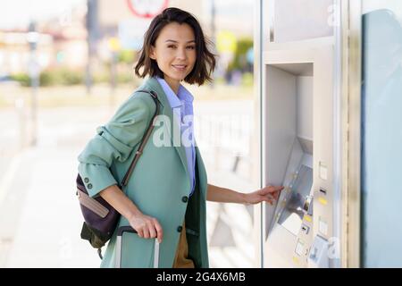 Femme souriante professionnelle achetant un billet de train à la gare Banque D'Images