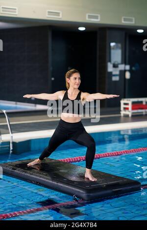 Femme aux bras débordés pratiquant le yoga sur le radeau dans la piscine Banque D'Images