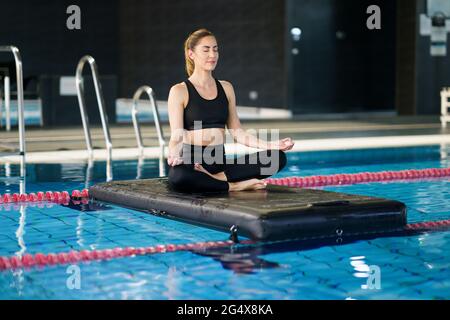 Femme pratiquant le yoga sur le radeau dans la piscine de la salle de gym Banque D'Images