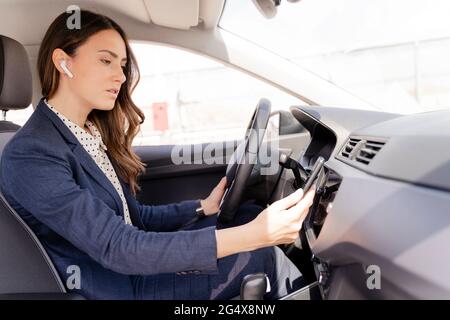 Femme d'affaires avec écouteurs intra-auriculaires utilisant un smartphone en voiture Banque D'Images