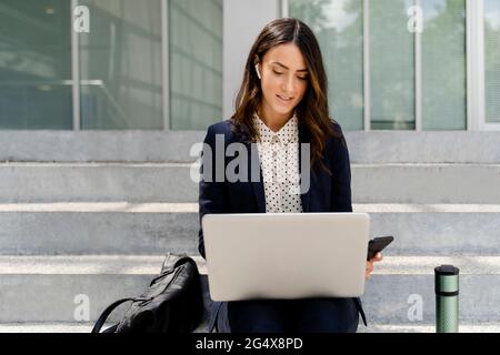 Femme d'affaires travaillant sur un ordinateur portable tout en étant assise sur un escalier Banque D'Images