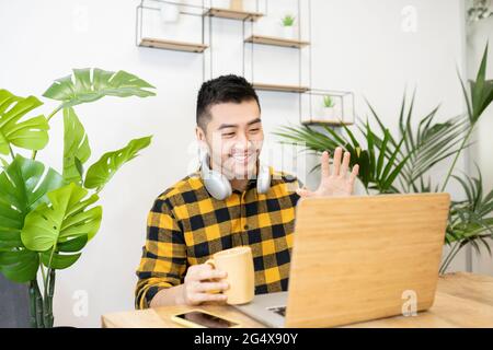 Souriant, un jeune homme professionnel agite tout en faisant des appels vidéo via un ordinateur portable au bureau Banque D'Images