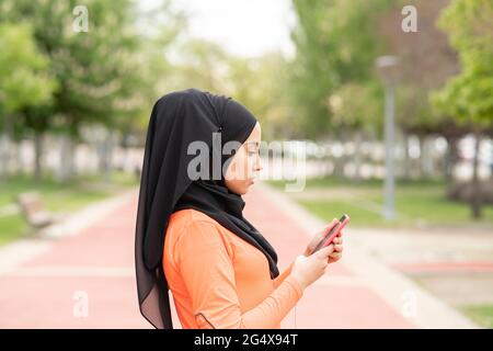 Femme arabe portant un foulard à l'aide d'un smartphone dans un parc public Banque D'Images