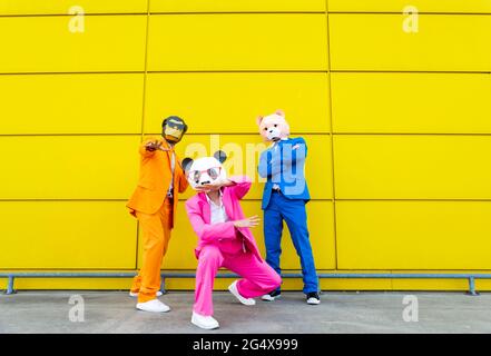 Trois adultes portant des costumes vibrants et des masques pour animaux se posant ensemble devant le mur jaune Banque D'Images