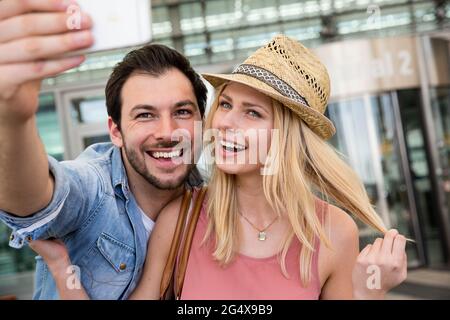 Un jeune couple prend le selfie par téléphone intelligent devant le terminal de l'aéroport Banque D'Images