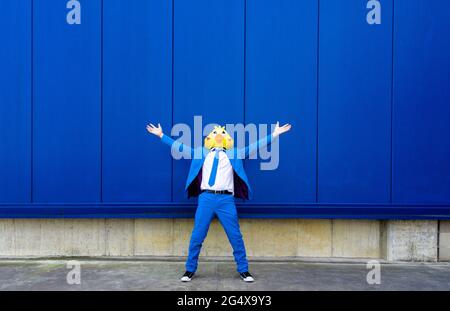 Homme portant un costume bleu vif et un masque d'oiseau debout à l'extérieur avec les bras relevés Banque D'Images