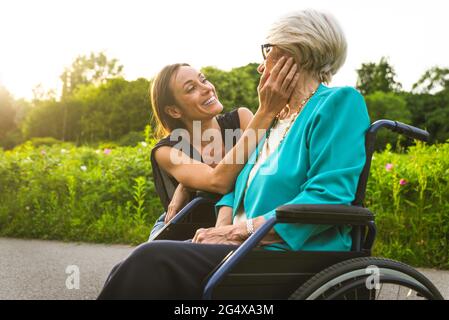 Petite-fille souriant en regardant la grand-mère assise en fauteuil roulant Banque D'Images