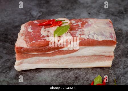 Morceau rouge et blanc de poitrine de porc crue avec ail sur fond sombre. Banque D'Images