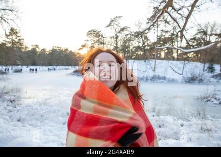 Joyeuse femme rousse enveloppée dans une couverture pendant l'hiver au coucher du soleil Banque D'Images