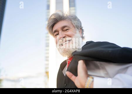 Homme d'affaires souriant portant une veste de costume sur l'épaule en ville Banque D'Images
