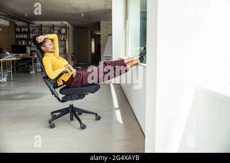 Femme d'affaires avec les pieds en haut se détendant sur une chaise au bureau Banque D'Images