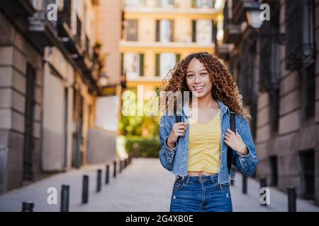 Femme souriante vêtue de vêtements en denim dans une allée près des bâtiments Banque D'Images