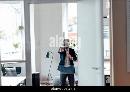 Homme d'affaires avec micro-casque de réalité virtuelle qui s'étire tout en restant debout au bureau Banque D'Images