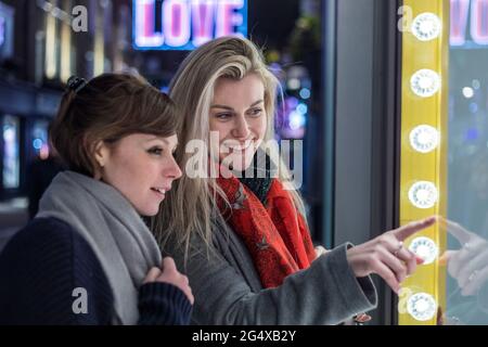 Jeunes femmes souriantes faisant des achats de fenêtre ensemble la nuit Banque D'Images