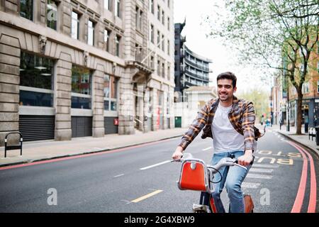 Un jeune homme souriant qui fait du vélo sur la route en ville Banque D'Images