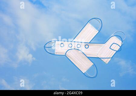 Modèle d'avion fait de masques de protection avec le contour de l'avion contre le fond d'un ciel bleu vif avec des nuages. Déplacement en toute sécurité en avion Banque D'Images