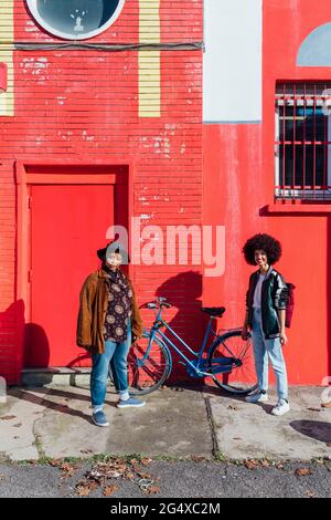 De jeunes amis debout à vélo devant le bâtiment Banque D'Images