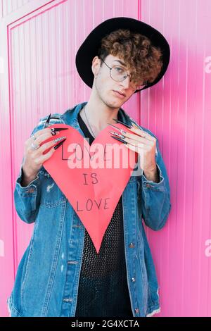 Jeune homme gay en forme de coeur, penché sur le mur rose Banque D'Images