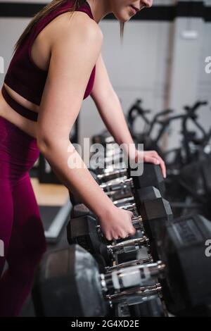 Sportswoman prenant l'haltère de la crémaillère tout en se tenant dans la salle de gym Banque D'Images