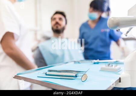 Équipements dentaires sur plateau avec des dentistes féminins et des patients masculins en arrière-plan à la clinique médicale Banque D'Images