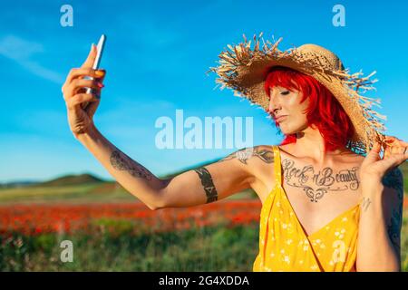 Femme avec les yeux fermés prenant selfie à travers le smartphone le jour ensoleillé Banque D'Images