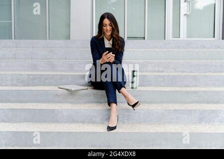 Femme entrepreneur utilisant le téléphone portable tout en étant assise sur l'escalier Banque D'Images