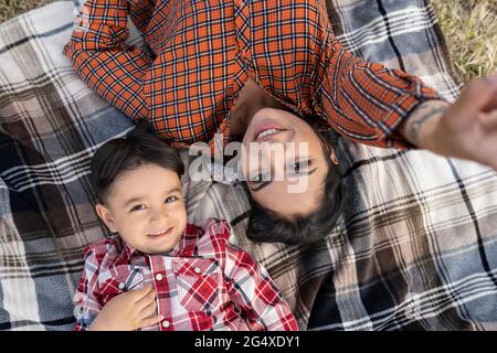 Mère souriante prenant le selfie avec son fils tout en étant allongé sur une couverture de pique-nique Banque D'Images