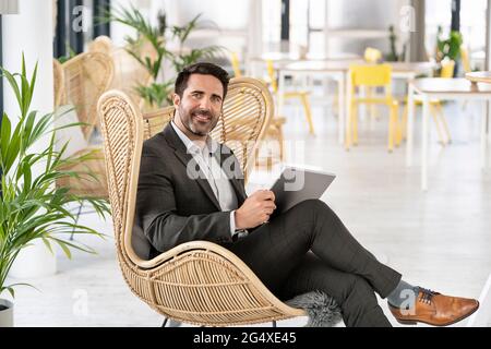 Homme d'affaires avec tablette numérique assis sur une chaise à la cafétéria dans le bureau Banque D'Images