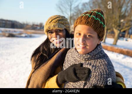 Mère et fils souriants portant un chapeau en tricot debout ensemble pendant l'hiver Banque D'Images