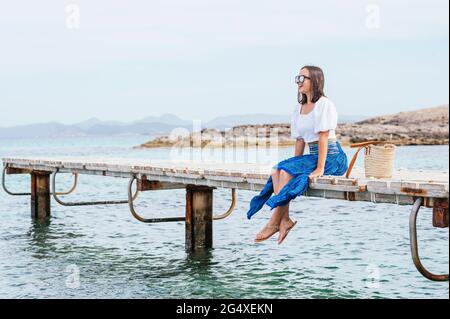 Bonne femme mûre portant des lunettes de soleil assis sur la jetée en regardant loin Banque D'Images