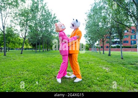 Couples adultes portant des costumes et des masques d'animaux vibrants qui embrassent le parc vert Banque D'Images