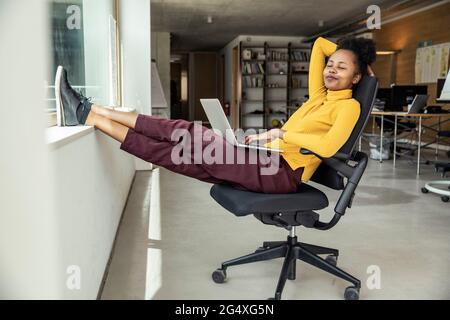 Femme d'affaires avec ordinateur portable se relaxant sur une chaise dans un appartement de bureau Banque D'Images