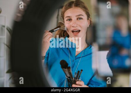 Adolescente utilisant des pinceaux de maquillage tout en se vlogant à la maison Banque D'Images