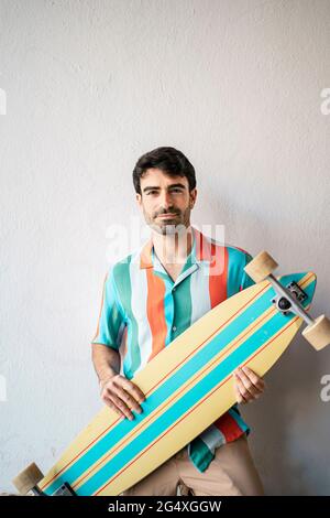 Jeune homme tenant une planche à roulettes sur un mur blanc Banque D'Images