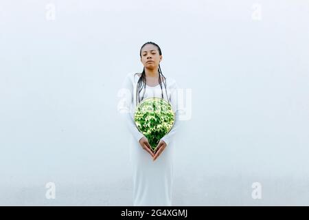 Jeune femme portant une robe blanche tenant un miroir devant le mur Banque D'Images