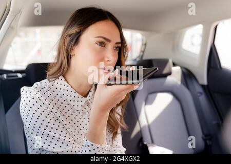 Femme d'affaires envoyant la messagerie vocale via un smartphone en étant assise dans la voiture Banque D'Images