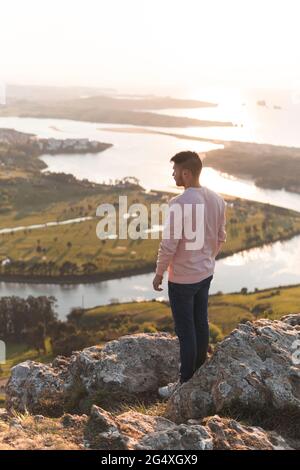 Jeune homme debout sur la falaise par beau temps Banque D'Images