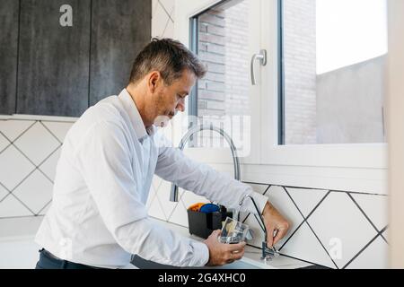 Homme d'affaires remplissant l'eau dans le verre à travers le robinet à la cuisine domestique Banque D'Images