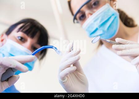 Dentiste féminin avec assistant tenant l'équipement dentaire à la clinique Banque D'Images