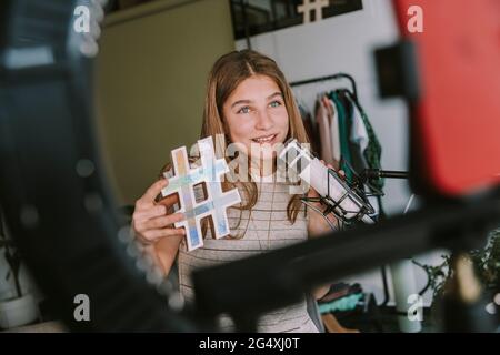 Fille tenant le symbole hashtag tout en vjournalisation à la maison Banque D'Images