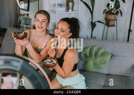 Les femmes entraîneurs de fitness mangeant des bols de fruits tout en vlogging à la maison Banque D'Images