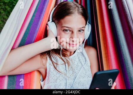 Une fille aux yeux bruns écoute de la musique tout en se relaxant dans un hamac multicolore Banque D'Images