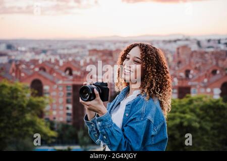 Jeune femme regardant loin tout en tenant l'appareil photo par la ville Banque D'Images