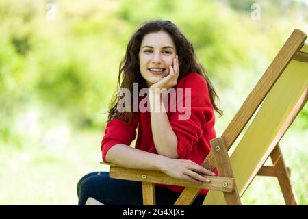 Jeune femme souriante, main sur le menton, assise sur une chaise Banque D'Images