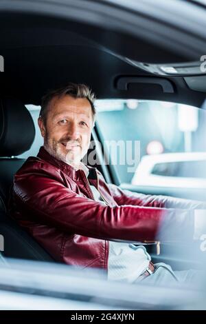 Homme mûr souriant assis sur le siège conducteur dans la voiture Banque D'Images