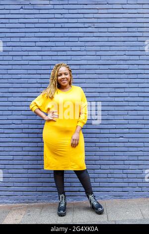 Femme assurée et de taille plus debout avec la main sur la hanche devant le mur en brique lavande Banque D'Images