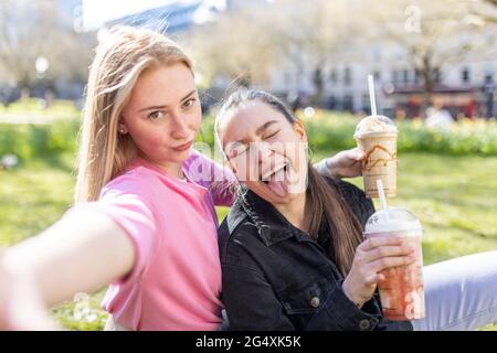 Jeune femme faisant un visage par une amie féminine tout en ayant Milk-Shake au parc Banque D'Images
